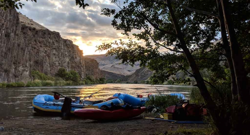 a few rafts rest on the shore of a river at sunset